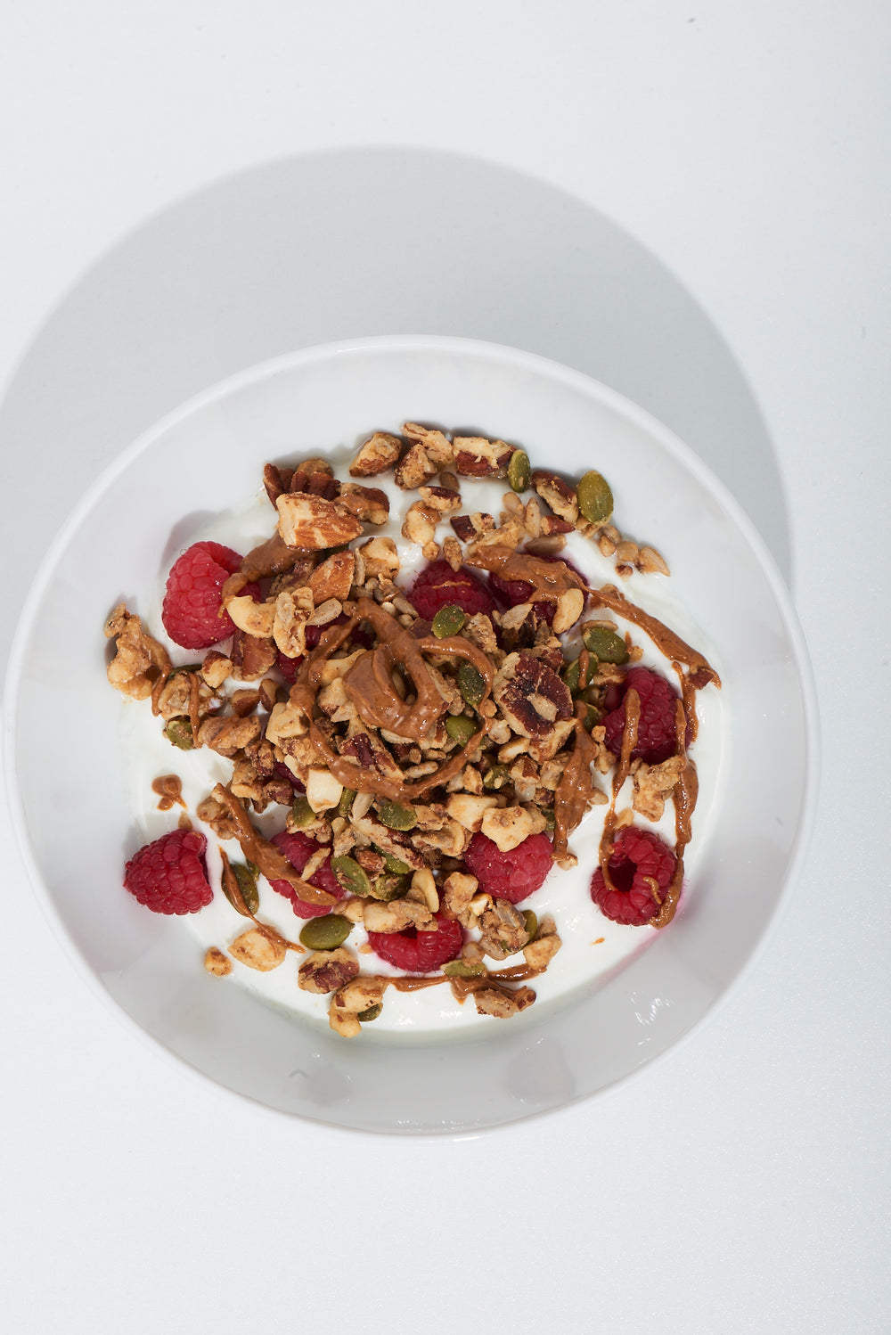 Bowl of granola with yogurt and raspberries on a white background