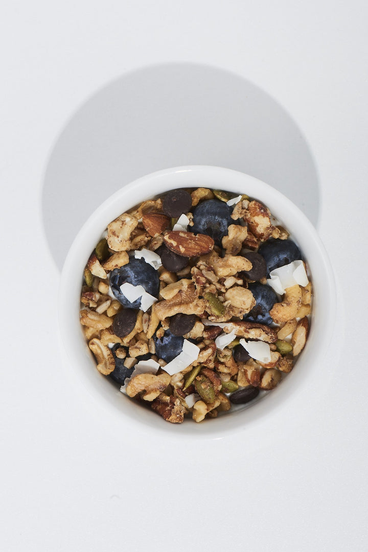 White container filled with granola, blueberries, and nuts on a white background