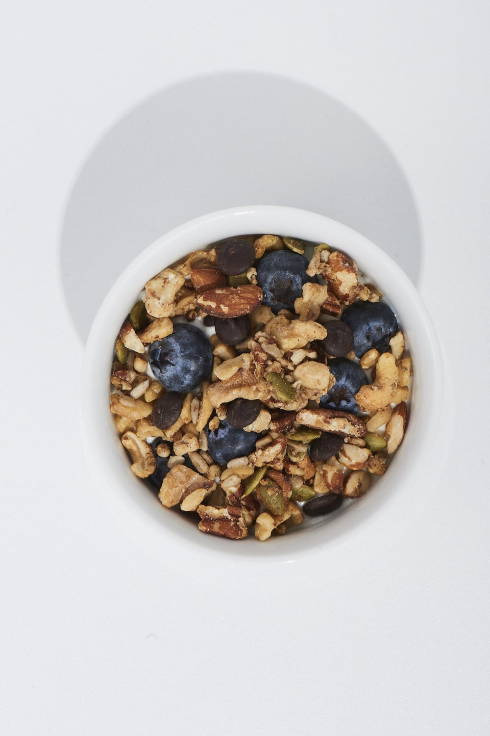 White container filled with granola, blueberries, and nuts on a white background
