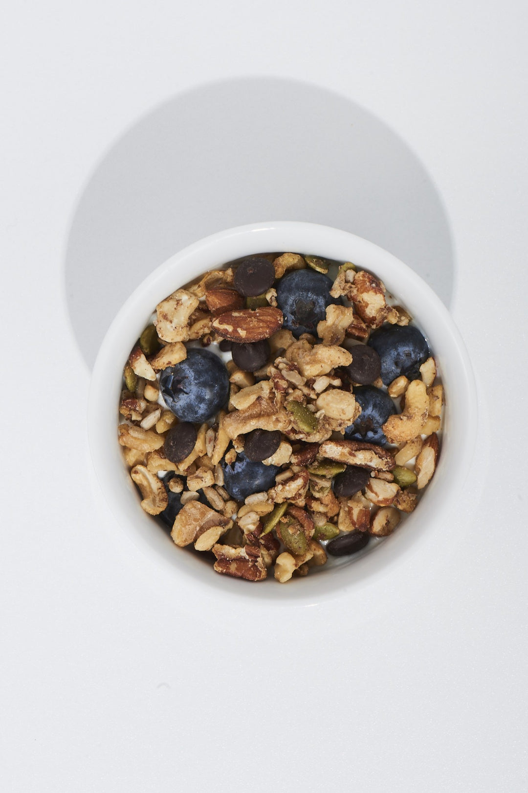 White container filled with granola, blueberries, and nuts on a white background