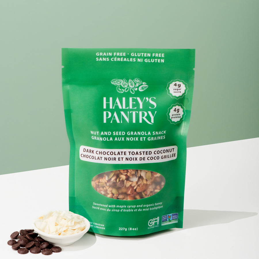 Green package of Haley's Pantry dark chocolate toasted coconut granola on a white surface with a light green background.